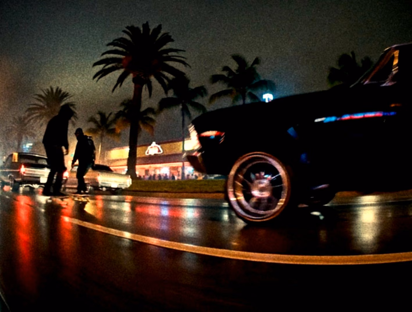 Lowriders crossing a rain soaked boulevard beneath palm trees