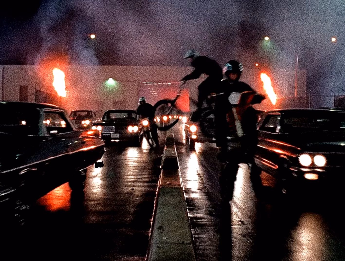 Riders and lowriders moving through a wet street at night