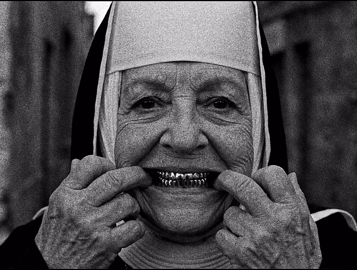 Monochrome close portrait of a smiling nun wearing metallic grillz