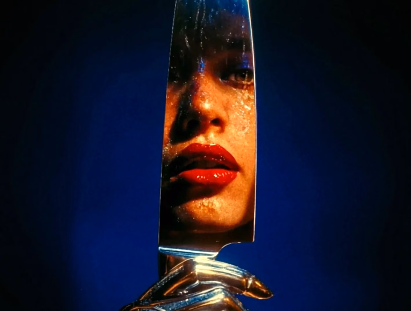 Woman reflected in a narrow chrome mirror against deep blue