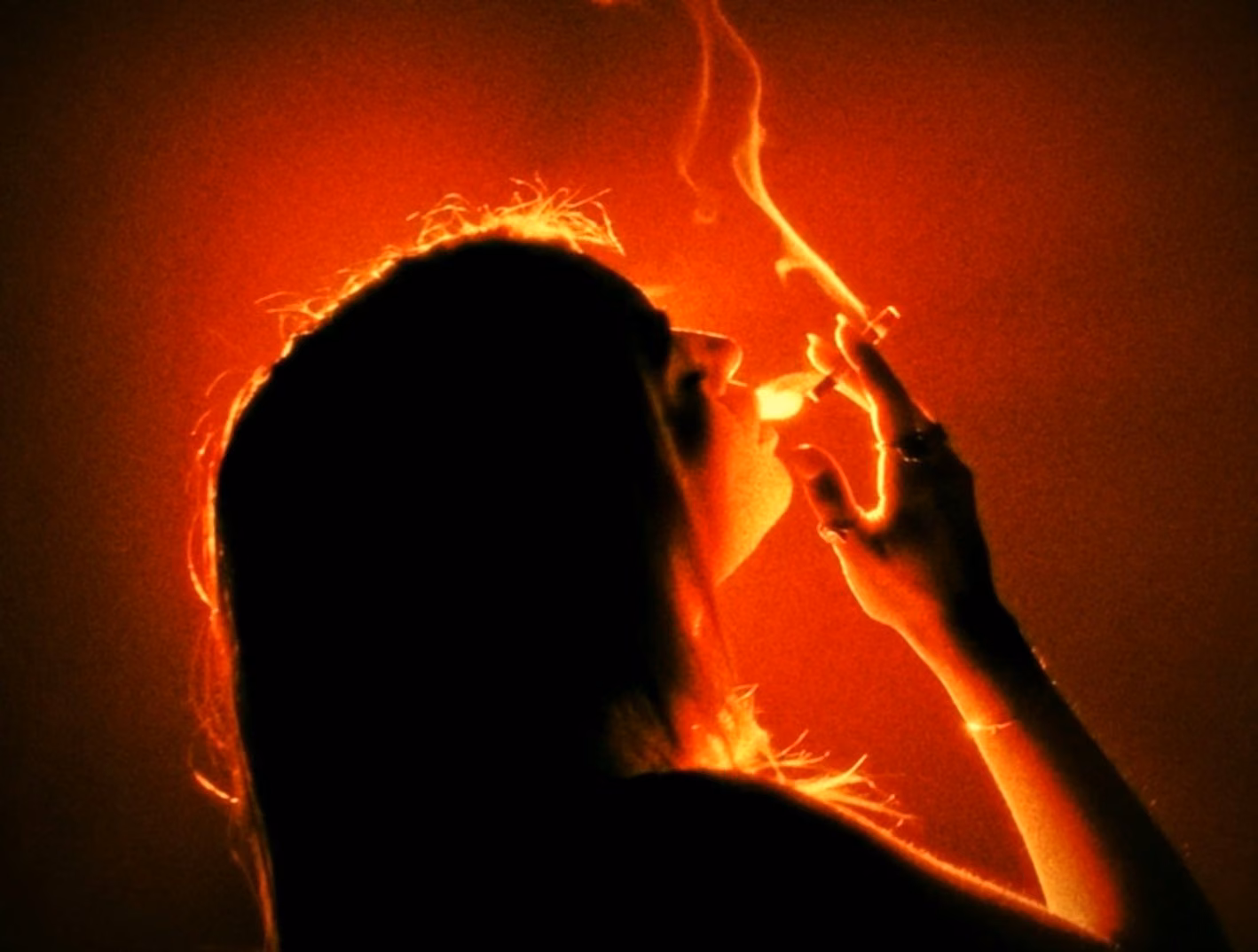 A woman smoking inside a red backlit haze