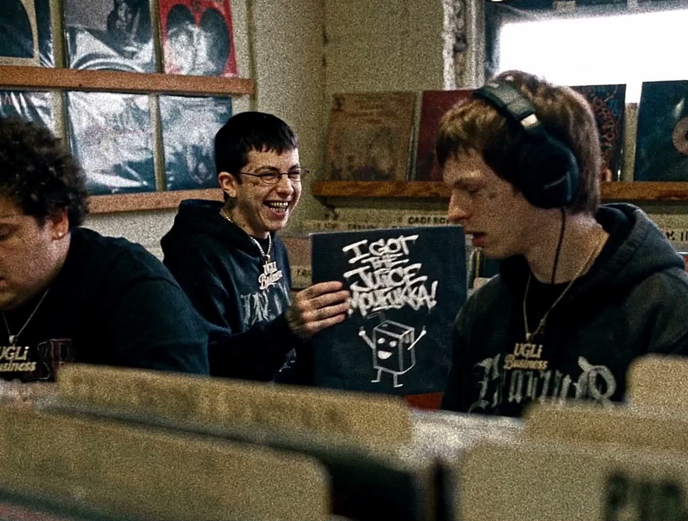 Three characters listening to records and holding the 2UGLi album sleeve in a record shop